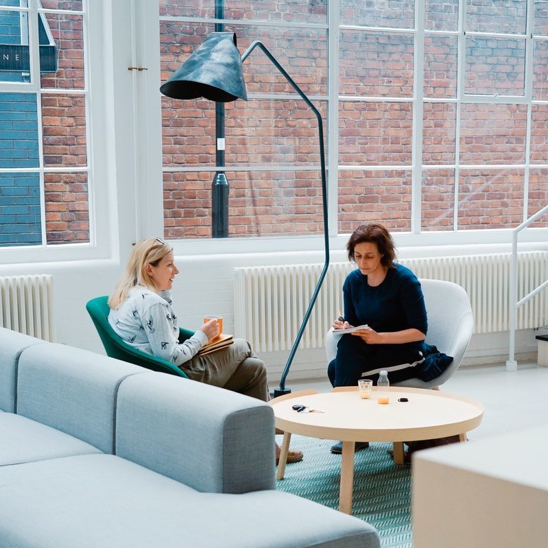 two woman sits on sofa chairs inside house