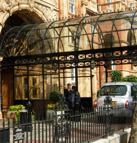 The entrance of The Landmark London hotel in Marylebone, featuring a glass canopy, black iron fencing, and a classic London taxi parked outside.