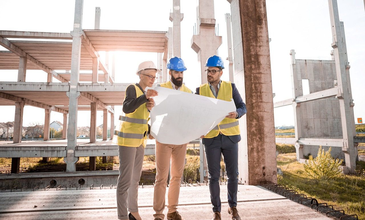 three men wearing hard hats and high vis jackets looking at plans on a construction site