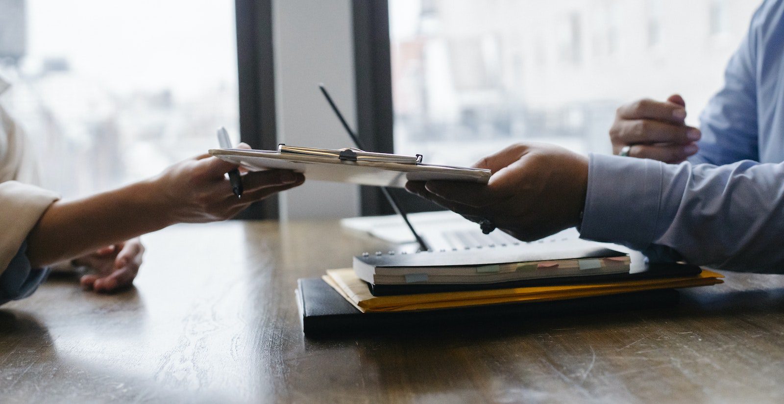 Crop anonymous ethnic woman passing clipboard to office worker with laptop during job interview