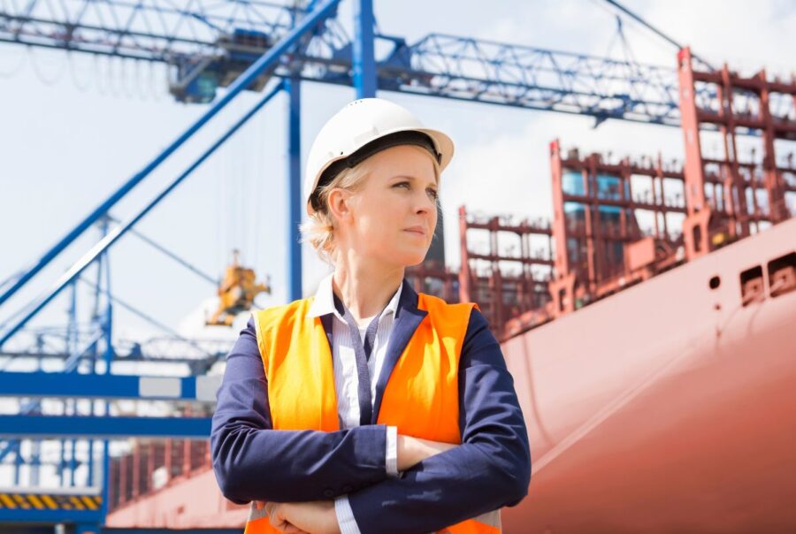 Female shipbuilder with arms folded in front of ship